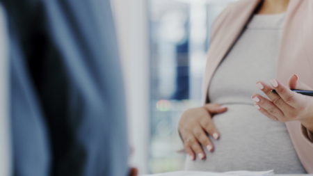 Pregnant woman talking to colleague while touching stomach
